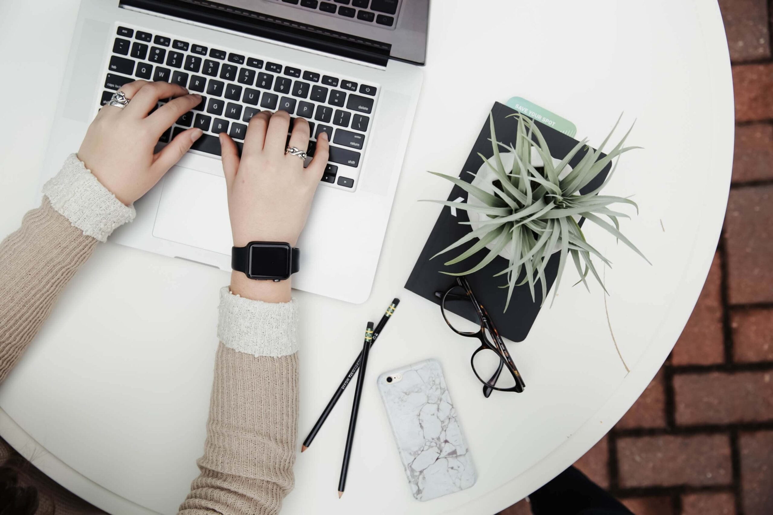 Overhead shot of a person typing on a laptop keyboard with a plant next to them.